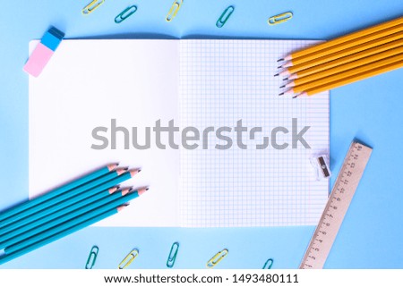 Notebook in a cage with a pencils, eraser, ruler, paper clips and other office supplies on a blue background. Concept back to school. Place for text.