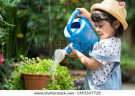 Asian little child girl pouring water on the trees. kid helps to care for the plants with a watering can in the garden. Royalty-Free Stock Photo #1493547728