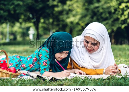 Portrait of happy muslim mother and little muslim girls child learning together with hijab dress smiling and enjoy relax reading and write a book in summer park.Education concept