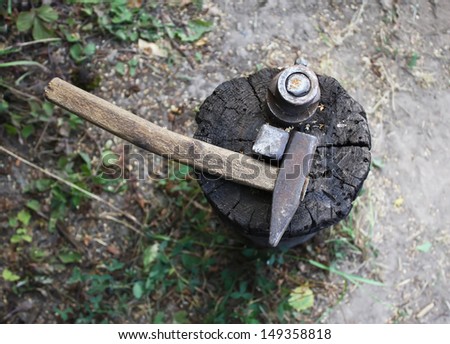 Hammer and iron tool for sharpening scythe on the tree stump