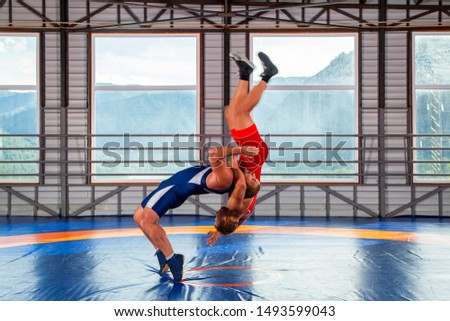 The concept of fair wrestling. Two greco-roman  wrestlers in sportwears makes a throw through the chest  on a wrestling carpet in the gym.The concept of male wrestling and resistance