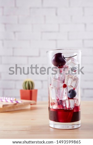 Pour the cherry sauce into a glass with ice and cherries. Placed on a light wood table White brick background 