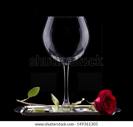 empty wine glass and red rose on black background