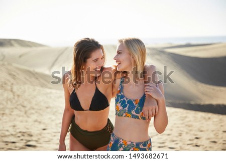 Beautiful young women in bikinis in sand, smiling