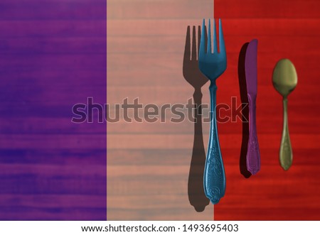 Colorful cutlery on a wooden table with French - France flag. 3D view on fork, knife and spoon. Perfect for restaurants.