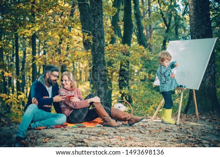 Mom and dad relax park picnic while kid painting. Rest and hobby concept. Parents relaxing while their son painting picture in nature. Art and self expression.