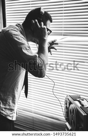 Special agent listens on the reel tape recorder. Officer wiretapping in headphones. Spying through the window. Old shutter blinds. Black and white photo.