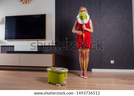 beautiful girl floor dancing with mop and bucket in evening dress and heel shoes in a cozy apartment with a TV in the hall.wife is waiting for her husband at home.funny mother cleaning company