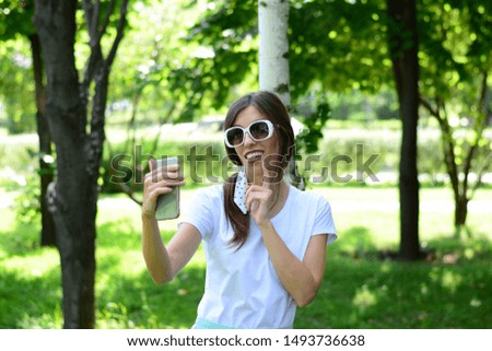 beautiful woman in sunglasses selfie on the phone in the park emotions white t-shirt logo sun