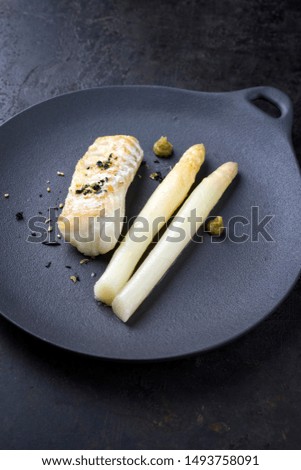 Fried Danish skrei cod fish filet with white asparagus, wasabi and nori as top view on a modern design plate with copy space 