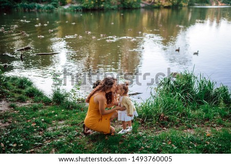 
young beautiful mother in a park on a lake with ducks kisses her little daughter. Against the background of a lake with ducks. horizontal photo