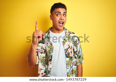 Young brazilian man on vacation wearing summer floral shirt over isolated yellow background pointing finger up with successful idea. Exited and happy. Number one.