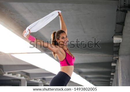 Athletic young woman with towel smiling and streaching. Young sporty woman training. Woman Doing Workout Exercises On Street . Fit girl streaching before active fitness training Royalty-Free Stock Photo #1493802005