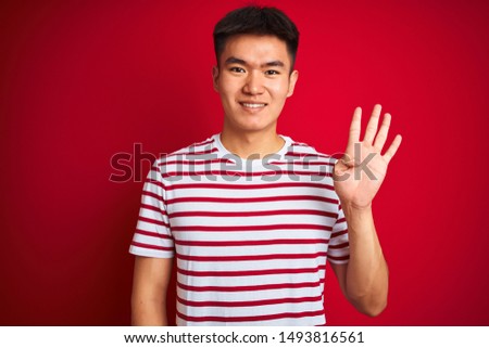 Young asian chinese man wearing striped t-shirt standing over isolated red background showing and pointing up with fingers number four while smiling confident and happy.