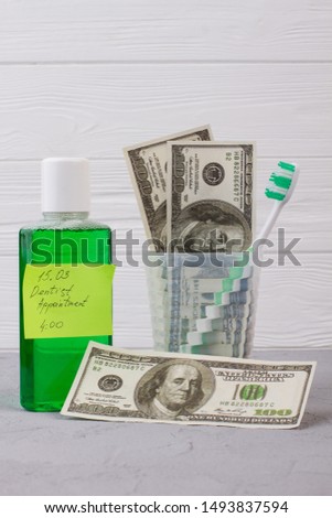 Oral hygiene tools, money and dentist appointment reminder. Mouthwash bottle, card with inscription Dentist appointment and American dollars banknotes.