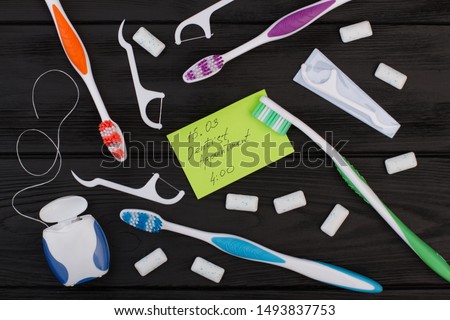 Dentist appointment message and tooth care products. Dentist appointment card, toothbrush, dental floss and chewing gums on black background.