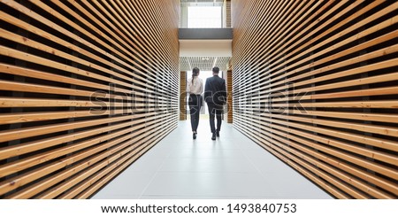 Two business people are walking in a modern office corridor in one direction Royalty-Free Stock Photo #1493840753