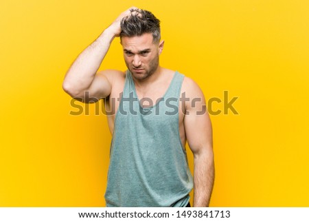 Young fitness man against a yellow background tired and very sleepy keeping hand on head.