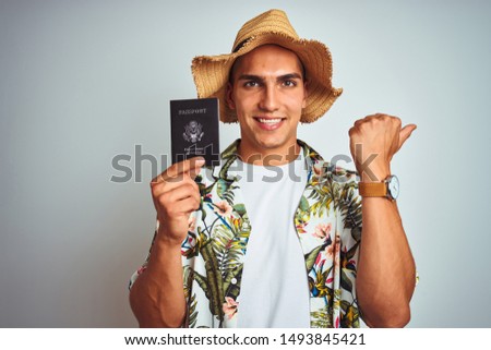 Young handsome man holding United States passport over white isolated background pointing and showing with thumb up to the side with happy face smiling