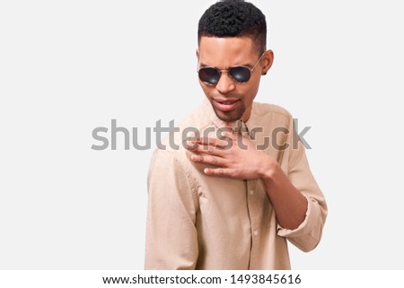 Horizontal studio portrait of African American man wearing round mirror sunglasses and casual beige shirt, making swag gesture and posing over white studio background. People emotion concept Royalty-Free Stock Photo #1493845616