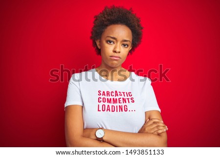 African american woman wearing sarcastic comments t-shirt over red isolated background skeptic and nervous, disapproving expression on face with crossed arms. Negative person.