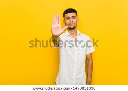 Young hispanic man standing with outstretched hand showing stop sign, preventing you.