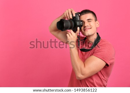 Young professional photographer taking picture on pink background. Space for text