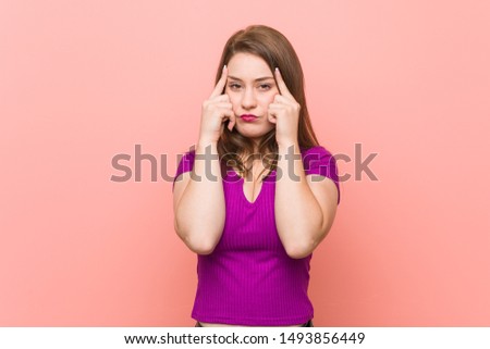 Young hispanic woman against a pink wall focused on a task, keeping forefingers pointing head.