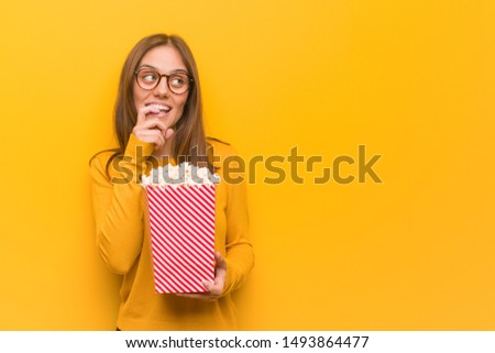 Young pretty caucasian woman relaxed thinking about something looking at a copy space. She is eating popcorns.