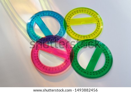 On a white background are four round protractors. Blue, yellow, purple and green.