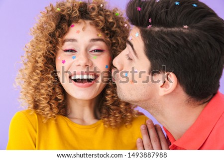 Image of cute content couple smiling and kissing on cheek while having party with glitter stars on faces isolated over violet background