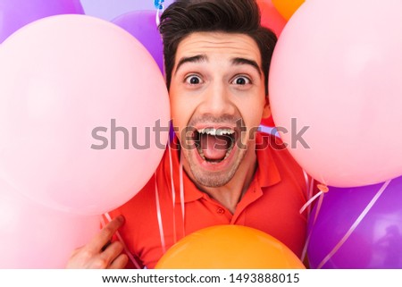 Image closeup of caucasian delighted man rejoicing while posing in multicolored air balloons isolated over violet background