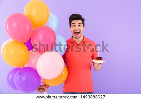 Image of positive joyful man celebrating birthday with multicolored air balloons and piece of pie isolated over violet background