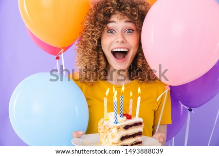 Image of excited young woman celebrating birthday with multicolored air balloons and piece of cake isolated over violet background