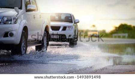 Cars run through flood water after hard rain with water spray from the wheels .Stop action ( capture with the high speed shutter) and selective focus.