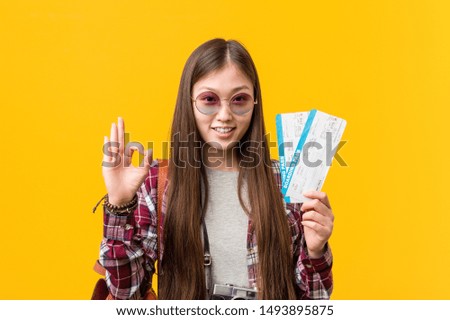 Young asian woman holding an air tickets cheerful and confident showing ok gesture.