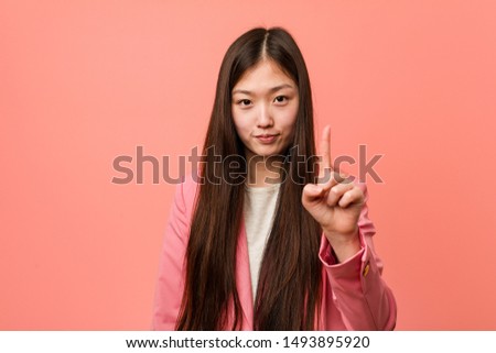 Young business chinese woman wearing pink suit showing number one with finger.