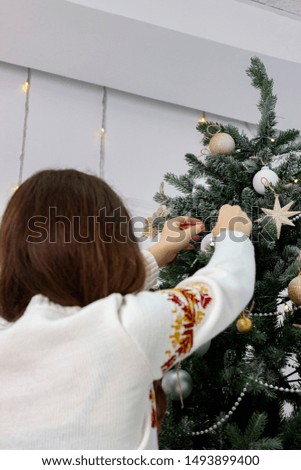 Girl in white warm sweater decorates christmas tree