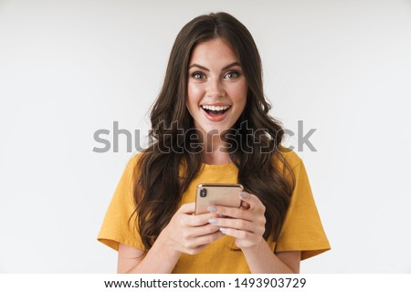 Photo of a shocked positive emotional surprised young woman posing isolated over white wall background using mobile phone.