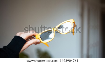 Close-up of female hand holding yellow glasses.