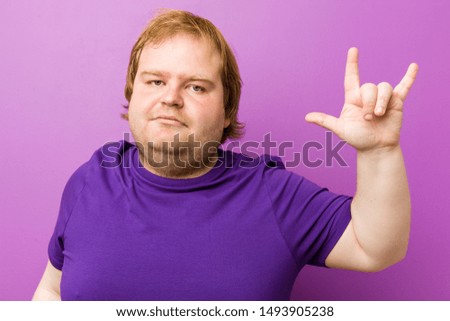 Young authentic redhead fat man showing a horns gesture as a revolution concept.