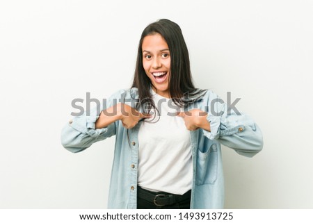 Young hispanic woman surprised pointing with finger, smiling broadly.