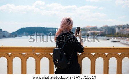 Young girl with backpack and pink hair, take a photo with smartphone from the bridge.