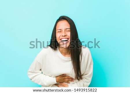 Young pretty hispanic woman laughs happily and has fun keeping hands on stomach.