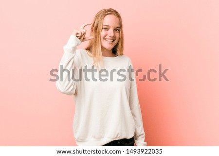 Young blonde teenager woman holding something little with forefingers, smiling and confident.