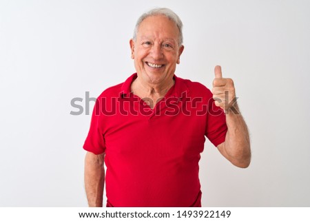 Senior grey-haired man wearing red polo standing over isolated white background doing happy thumbs up gesture with hand. Approving expression looking at the camera with showing success.