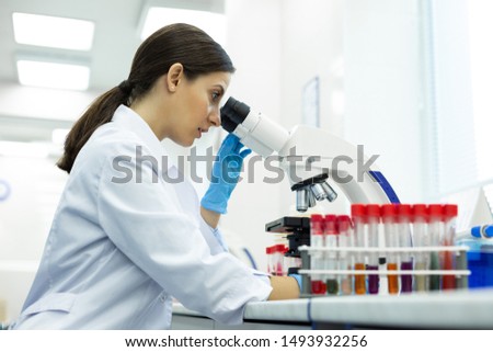 Just attention. Pretty young pharmacist sitting in semi position and examining test tubes with colorful liquid