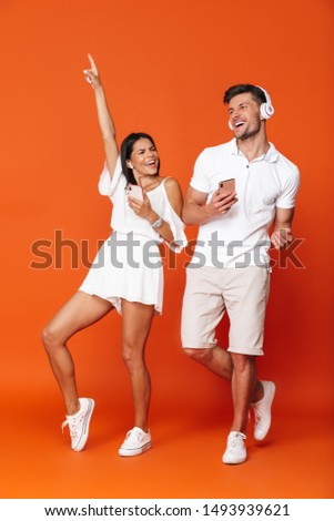 Picture of a positive optimistic emotional smiling young amazing loving couple posing isolated over red wall background using mobile phones listening music with headphones.