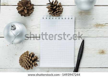 Empty notebook, pen, Christmas balls, fir cones on a white wooden background