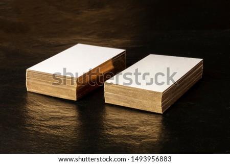A mockup for two stacks of white business cards with gold painted edges on a black background, with a place for text